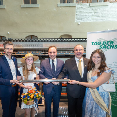 Bild vergr&ouml;&szlig;ern: Der Sebnitzer Oberbürgermeister Ronald Kretzschmar übergibt den Staffelstab zusammen mit dem Blumenmädchen und Landtagspräsident Alexander Dierks an Plauens OB Steffen Zenner und die Spitzenprinzessin (v.l.n.r.)